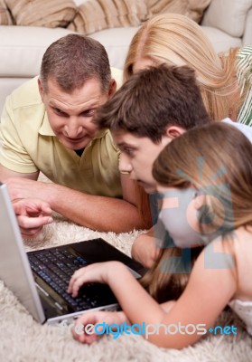 Domestic Family Of Four Lying And Working With Laptop Stock Photo