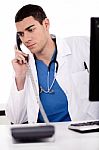 Male Doctor Sitting At The Desk Talking Over Phone Stock Photo
