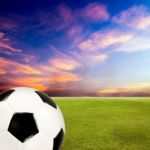 Soccer Ball With Green Grass Field Against Sunset Sky Stock Photo