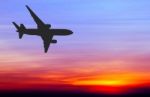 Silhouetted Commercial Airplane Flying At Sunset Stock Photo