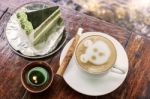 Cappuccino Coffee With Cinnamon Stick And Green Tea Cake On Table With Candle Stock Photo