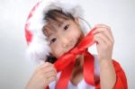 Asian Little Girl Dressed In Santa Claus Holding Red Ribbon Stock Photo