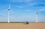 Farmer On Tractor Sowing In Soil Near Dike And Windmills Stock Photo