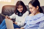 Asian Girl In Blue Casual Dress Listening To Music From Black Headphones And Use Laptop. In A Comfortable And Good Mood, In The Living Room On The Sofa Stock Photo