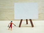 Miniature Little Boy Standing Near An Easel On Wooden Background Stock Photo