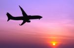 Silhouetted Commercial Airplane Flying At Sunset Stock Photo