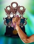 Hand Holding Gold Medal With Golden Cup Of Championship Behind Stock Photo