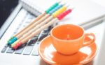 Laptop With Coffee Cup And Notepad On Desk Stock Photo