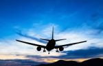 Silhouetted Commercial Airplane Flying At Sunset Stock Photo