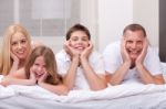 Beautiful Family Lying On Bed Smiling And Looking At You Stock Photo