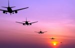 Silhouetted Commercial Airplane Flying At Sunset Stock Photo