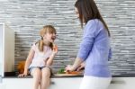 Young Woman And Little Girl Eating Carrots In The Kitchen Stock Photo