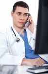 Portrait Of Male Physician Holding Receiver And Looking The Computer Stock Photo