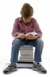 Front View Of Boy Sitting On Books On White Background Stock Photo