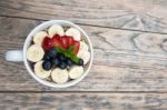 Acai Bowl With Fresh Fruit Strawberry, Blueberry, Banana And Peppermint Leaves On Top On The Wooden Table Stock Photo