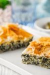 Greek Pie Spanakopita On The White Plate With Blurred Accessorizes Stock Photo