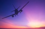 Silhouetted Commercial Airplane Flying At Sunset Stock Photo