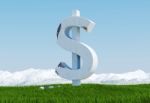 Damaged Concrete Dollar Sign Statue Isolated On Grass Meadow With Snowy Mountain And Blue Sky As Background Stock Photo