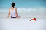 The Hat Is Beside Woman Sitting On The Beach Stock Photo