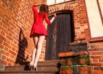 Young Woman In Red Dress Is Standing With Her Back On The Stairs Stock Photo