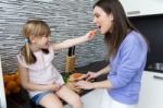 Young Woman And Little Girl Eating Carrots In The Kitchen Stock Photo