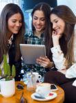 Three Young Woman Using Digital Tablet At Cafe Shop Stock Photo