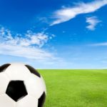 Soccer Ball With Green Grass Field Against Blue Sky Stock Photo