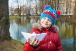 Little Girl Holding A Paper Boat Near The River Stock Photo