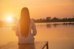 Silhouette Of Relaxing Young Woman On Wooden Pier At The Lake In Sunset Stock Photo