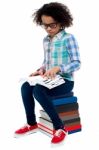 Young Kid Sitting On Stack Of Books And Reading Stock Photo