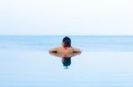 Woman Looking Out From Infinity Swimming Pool Stock Photo