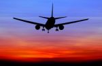 Silhouetted Commercial Airplane Flying At Sunset Stock Photo