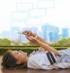 City Life Style Of Asian Woman Lying And Touching On Mobile Phone Screen Against Green Environment And Urban Skylind Background Stock Photo