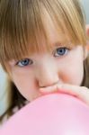 Cute Little  Girl Inflating A Pink Balloon In The Kitchen Stock Photo