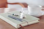 Notebook With Pen, Eyeglasses And White Coffee Cup On Wooden Tab Stock Photo