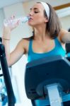 Young Woman With Elliptic Machine Drinking Water In The Gym Stock Photo