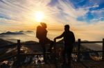 Silhouette Of Young Woman And Man With Backpacks And Sticks On Mountains At Sunset Stock Photo