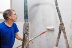 Elderly Worker Painting Wall With Glue Stock Photo