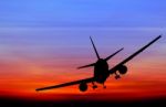 Silhouetted Commercial Airplane Flying At Sunset Stock Photo