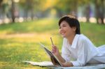 Young Woman Lying On Green Grass Park With Pencil And Note Book Stock Photo