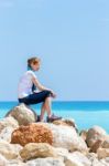 Caucasian Woman Sitting On Rocks At Coast Near Sea Stock Photo