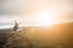 Backpacker Woman Relaxing And Victory Hand Rising On Rock Cliff And Sun Set Sky Above Stock Photo