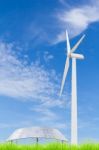 Solar Panels And Wind Turbine On Green Grass Field Against Blue Stock Photo