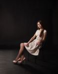 Young Beautiful Girl In A Bright Dress Sitting On The Chair Stock Photo