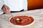 Chef Baker Spreading Sauce On Pizza Base Stock Photo