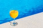 Glass With Orange Juice On Edge Of Swimming Pool Stock Photo