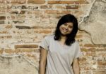 Girl Posing And Smiling While Standing Near Brick Wall Stock Photo