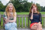 Two Girls On Bench In Park Calling Mobile Stock Photo