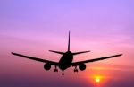 Silhouetted Commercial Airplane Flying At Sunset Stock Photo