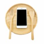 Top View Smartphone On Wooden Dish With Spon And Fork On White Background, Concept Eating Technology Stock Photo